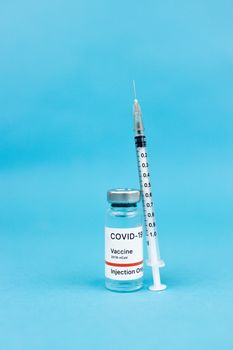 Clear shot of COVID-19 vaccine vial with syringe against a blue backdrop, symbolizing medical advancement.