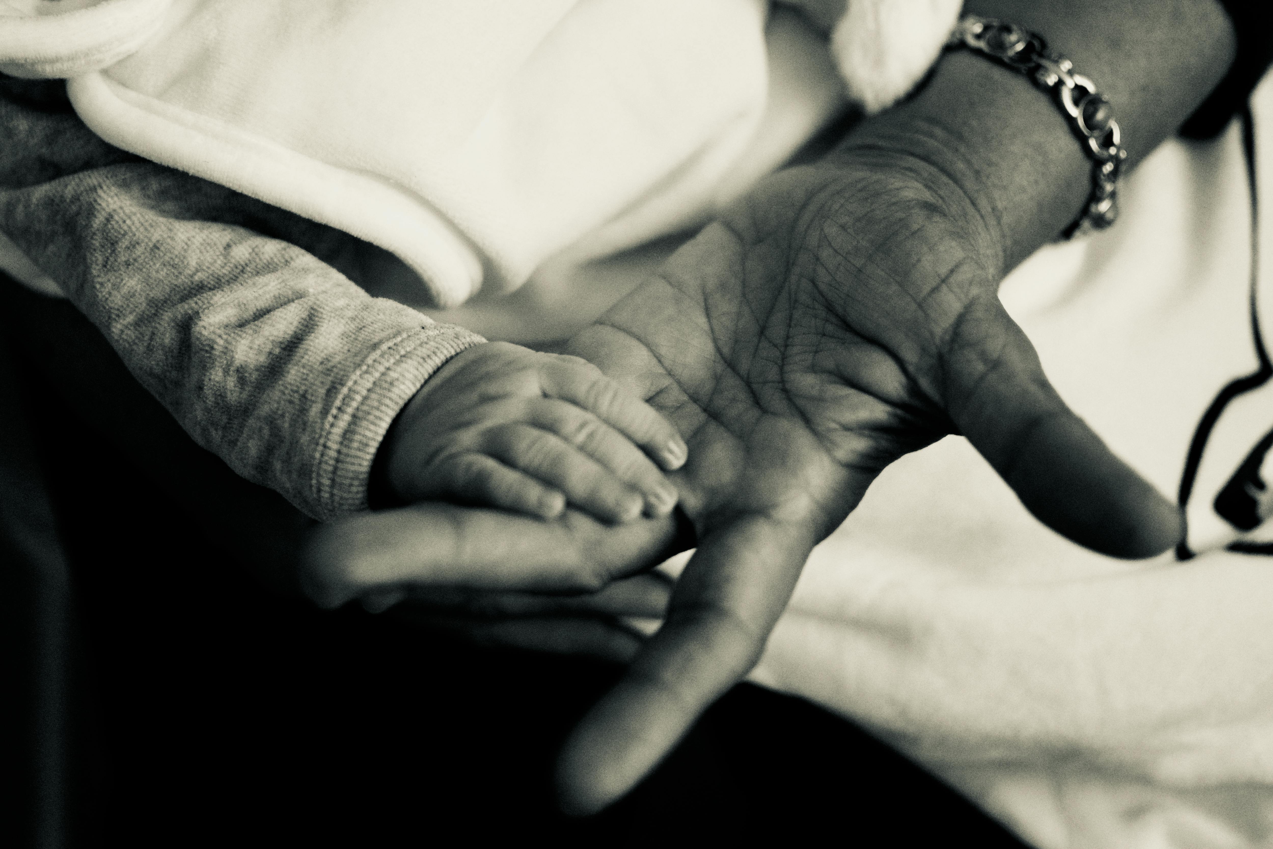 Touching black and white photo of a baby's hand grasping an elderly palm, symbolizing connection.