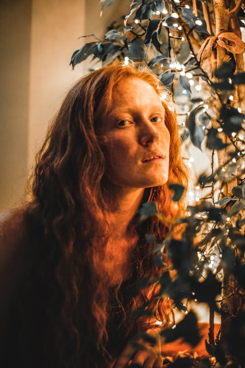 Dreamy redhead woman near glowing plant at home