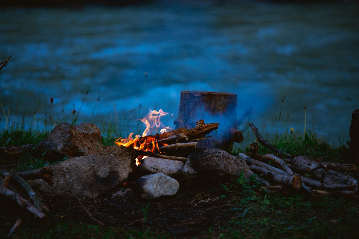 A small campfire burning among rocks at the water's edge at twilight beside a calm lakeshore