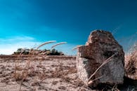 广阔的沙漠上，明亮的蓝天下，孤零零地立着岩石和干草