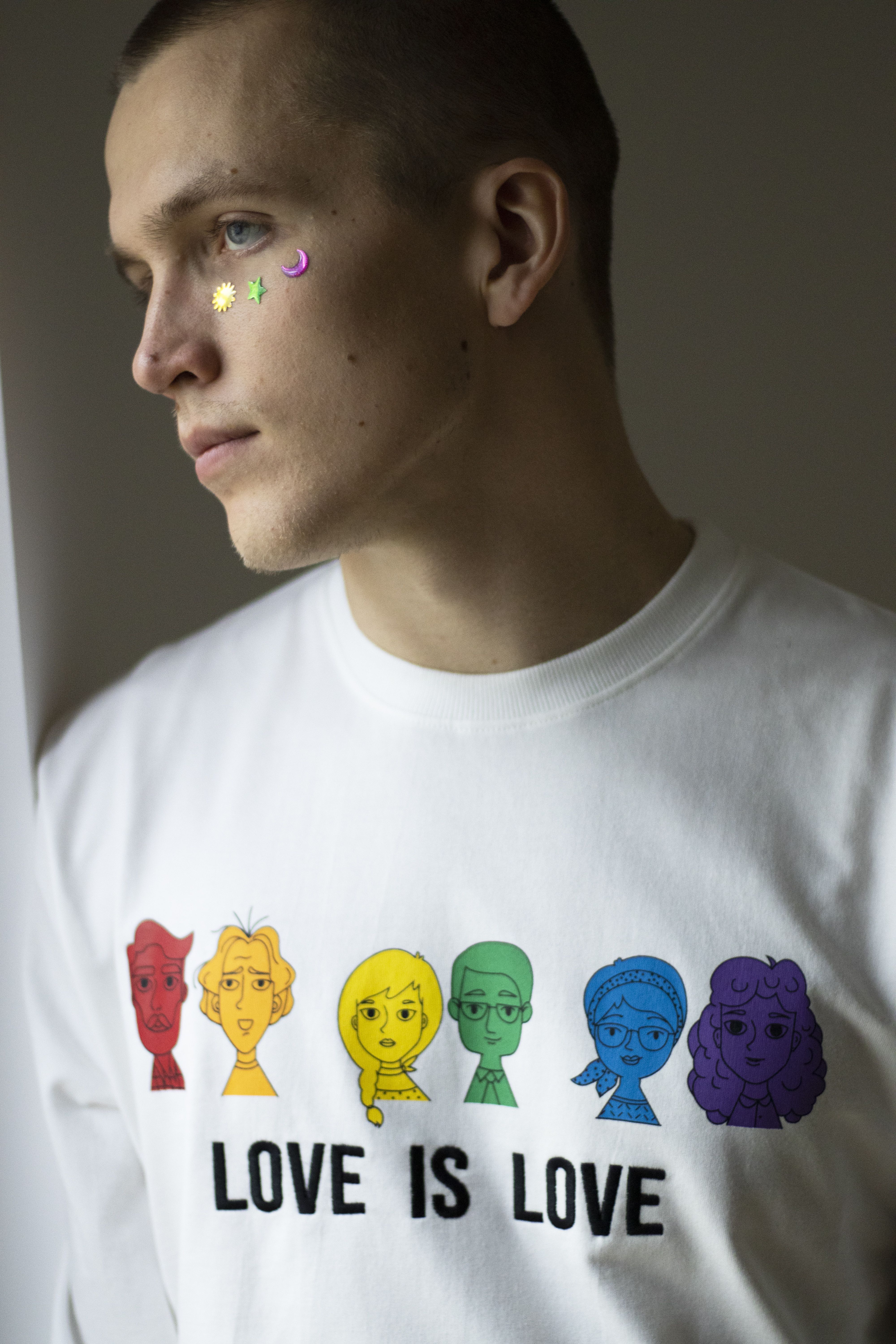 Close-up of a man wearing a 'Love is Love' shirt, adorned with star stickers, symbolizes LGBT pride.