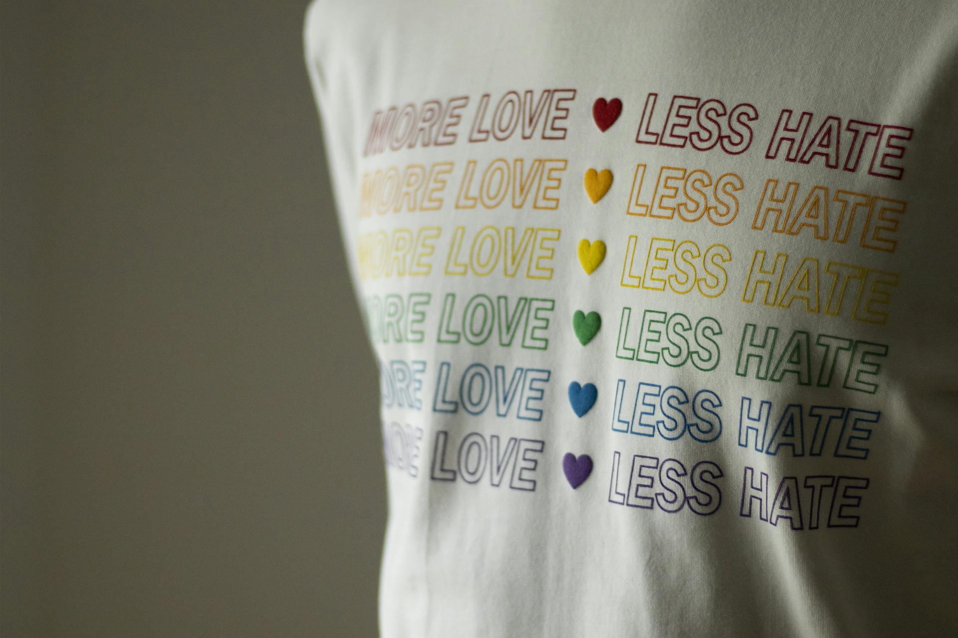 Close-up of a shirt with 'More Love Less Hate' slogan in rainbow colors, promoting LGBTQ pride.