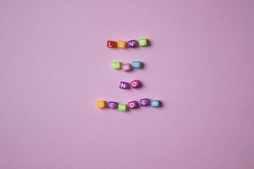 Colorful beads spelling 'Love Has No Gender' on a pink background, emphasizing inclusivity.