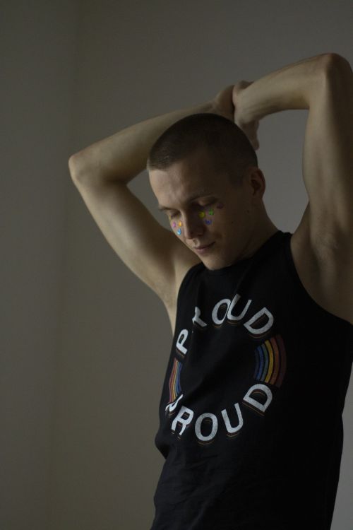 Free A man confidently posing with raised arms in a black tank top labeled 'Proud' in a studio setting. Stock Photo