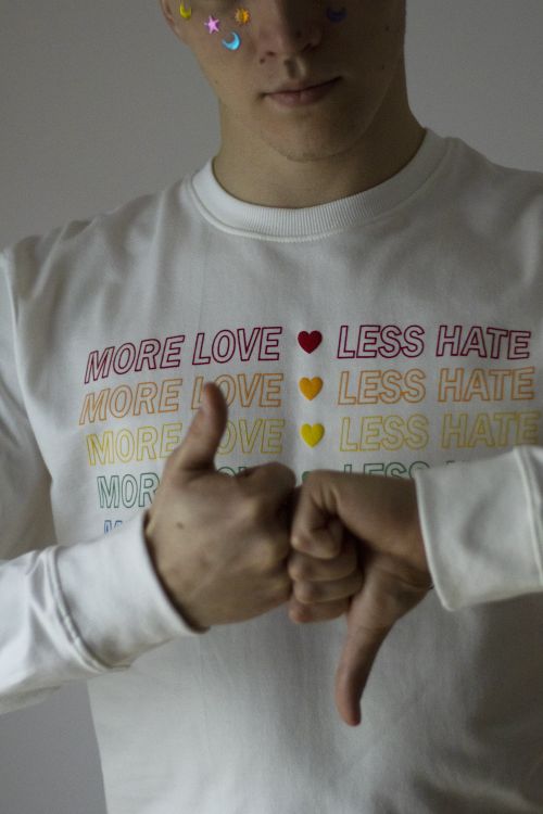 Free Close-up of person expressing pride with a thumbs up and down gesture on a 'More Love, Less Hate' shirt. Stock Photo
