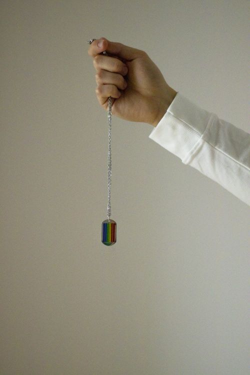 Free A hand holds a rainbow pendant, symbolizing LGBTQ pride on a minimalist background. Stock Photo