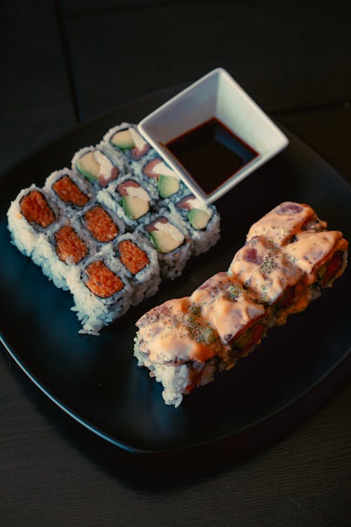 High angle of various palatable sushi rolls on plate near sauce in kitchen