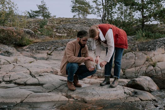 Outdoor couple enjoying coffee on rocky terrain, embracing nature in stylish attire.