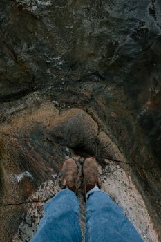 A traveler in blue jeans stands on a rugged cliff overlooking the water.