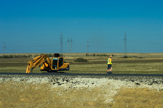 Man working on a road construction site with an excavator outdoors.