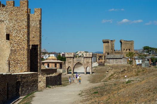 People walking among the ruins of an ancient fortress under a clear blue sky.