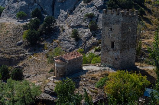 Stone tower amidst rocky terrain with green scattered trees and bright daylight.