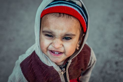 Free A young child with a beanie and hoodie squinting and smiling on a chilly day. Stock Photo