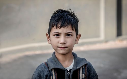 Free A young boy wearing a gray sweater poses outside against a concrete wall. Stock Photo