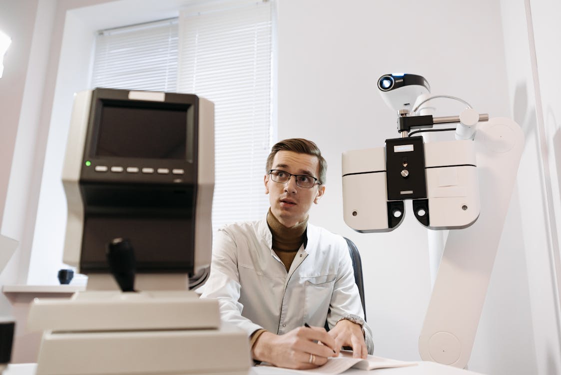 Free Man in White Holding a Pen Sitting Near a Medical Equipment Stock Photo, 