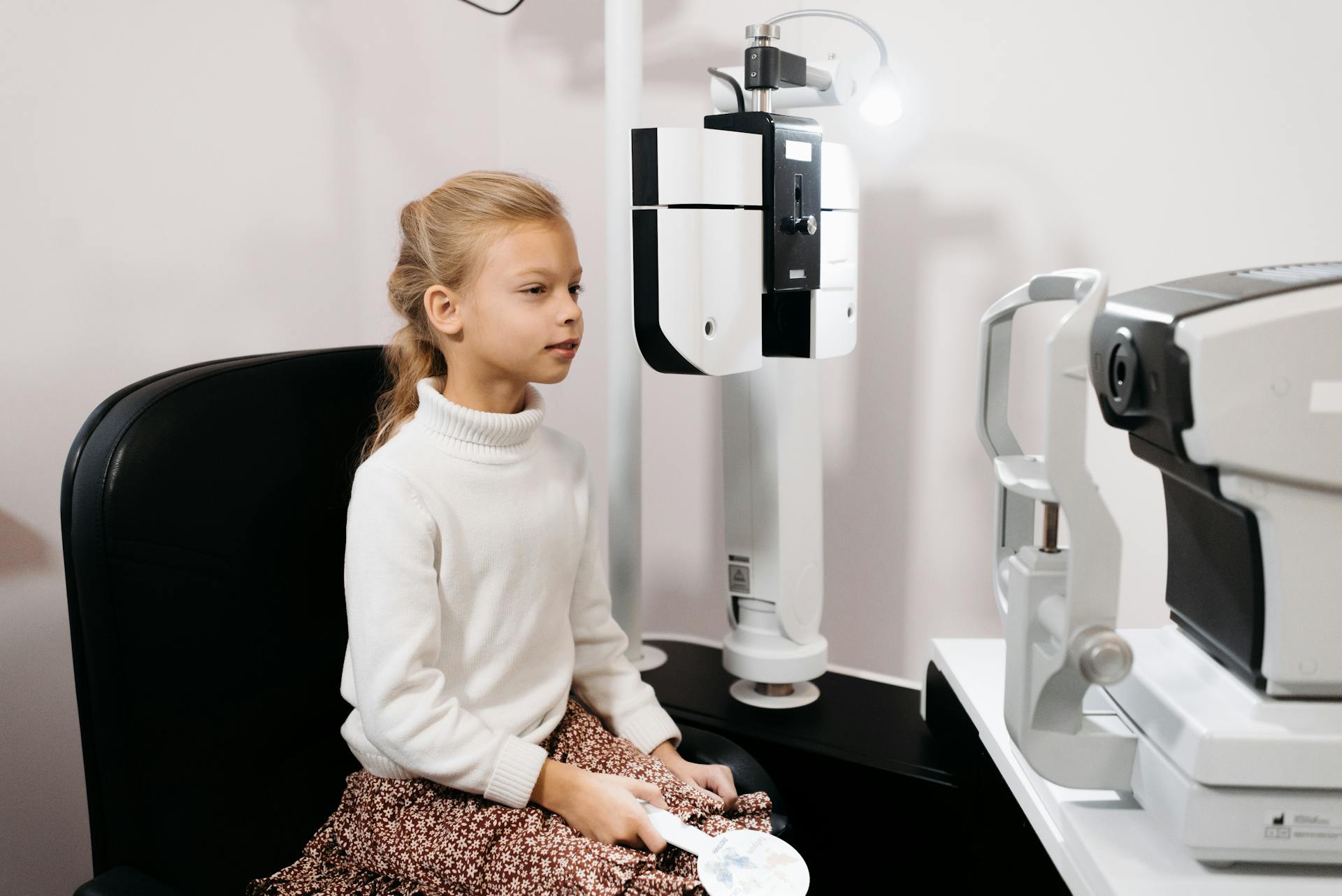 A young girl sits for an eye test using optical instruments in a medical facility.