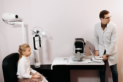 A young girl sits for an eye exam with an optometrist using digital equipment.