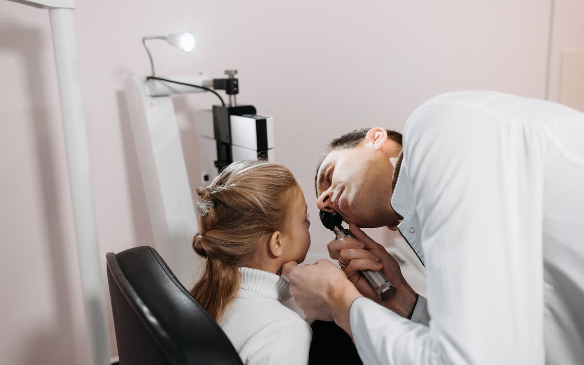A doctor examines a young girl's ear during a medical appointment in a clinic.