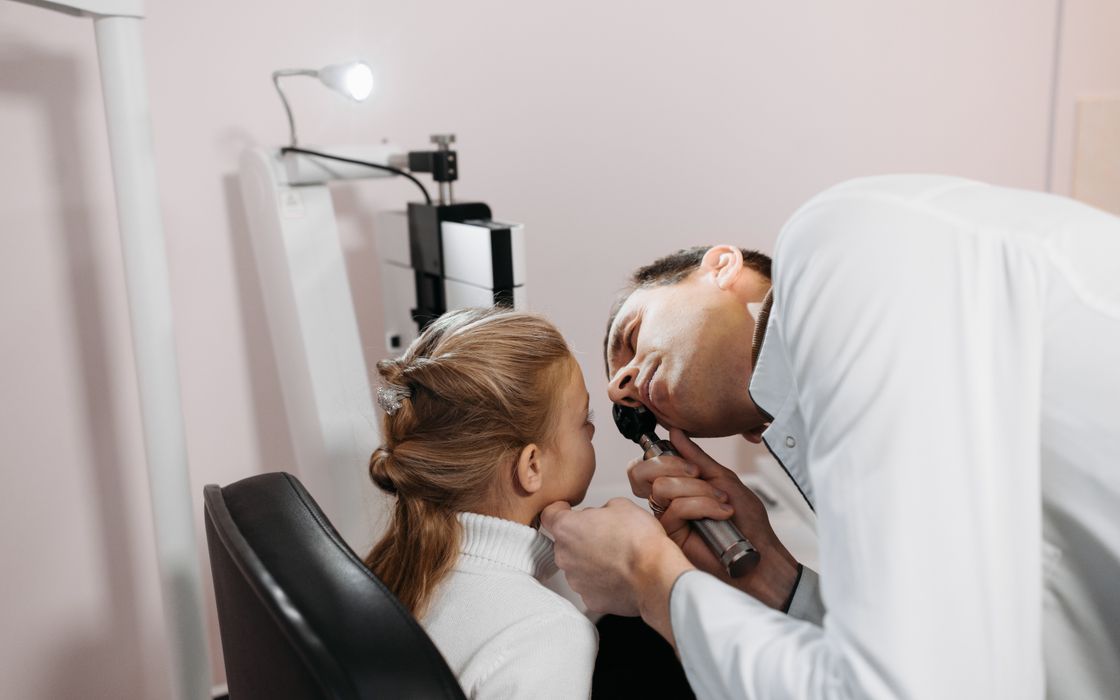 A doctor examines a young girl's ear during an appointment in a clinic.