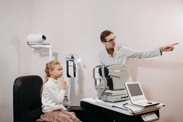 Doctor examining a young girl's eyes with clinic equipment
