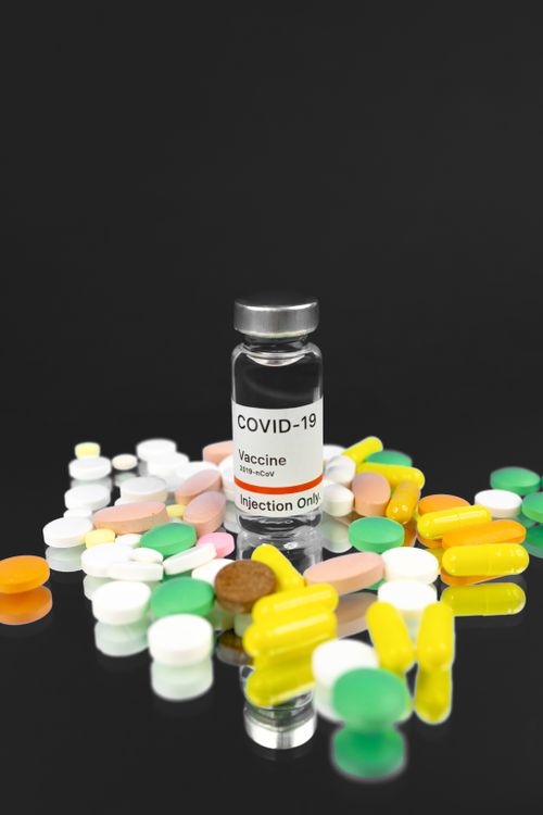 Free Conceptual image of COVID-19 vaccine surrounded by colorful pills representing treatment and healthcare solutions. Stock Photo
