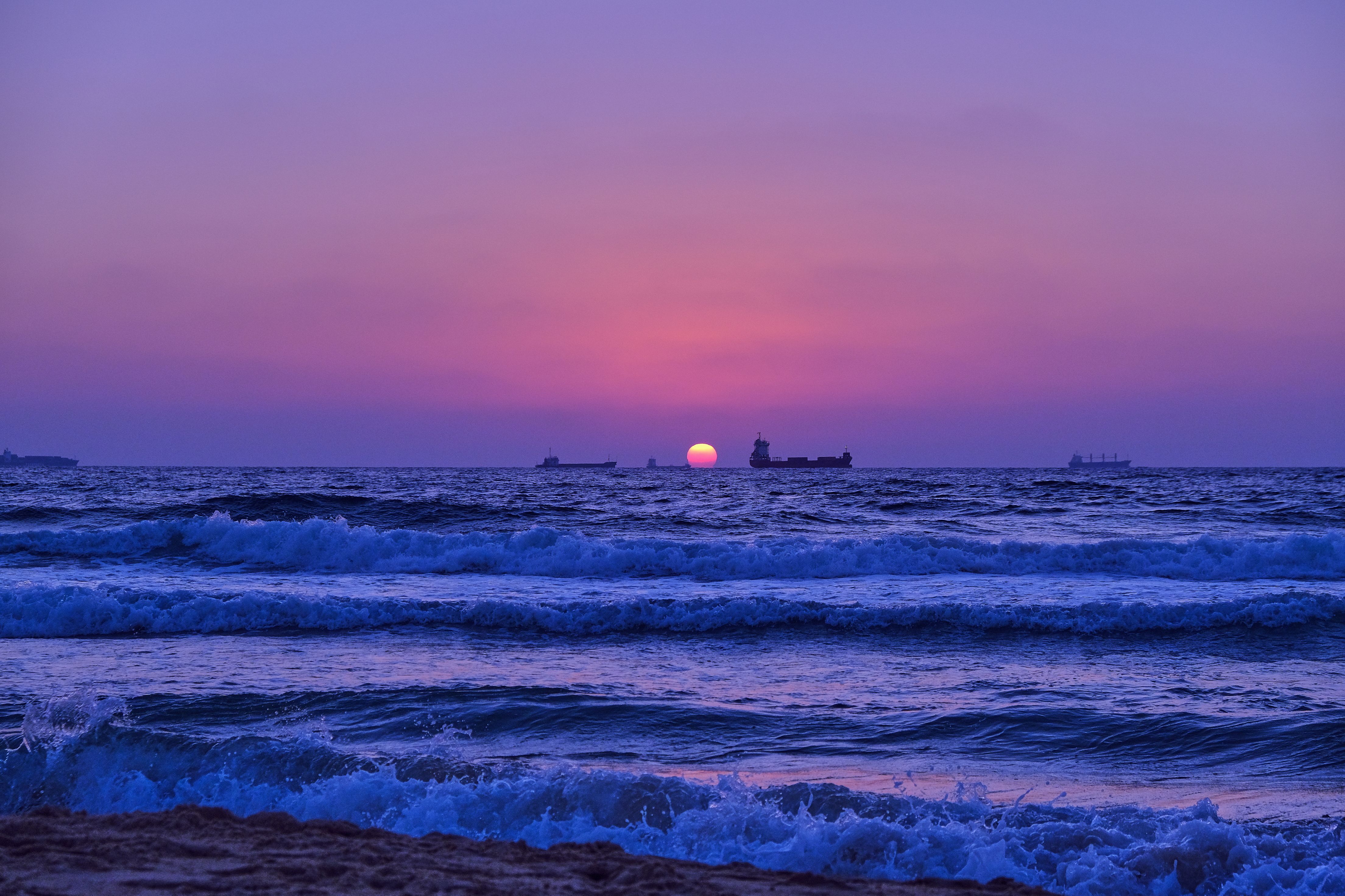 A stunning purple sunset over the sea in Ashdod, Israel, with waves and vessels on the horizon.