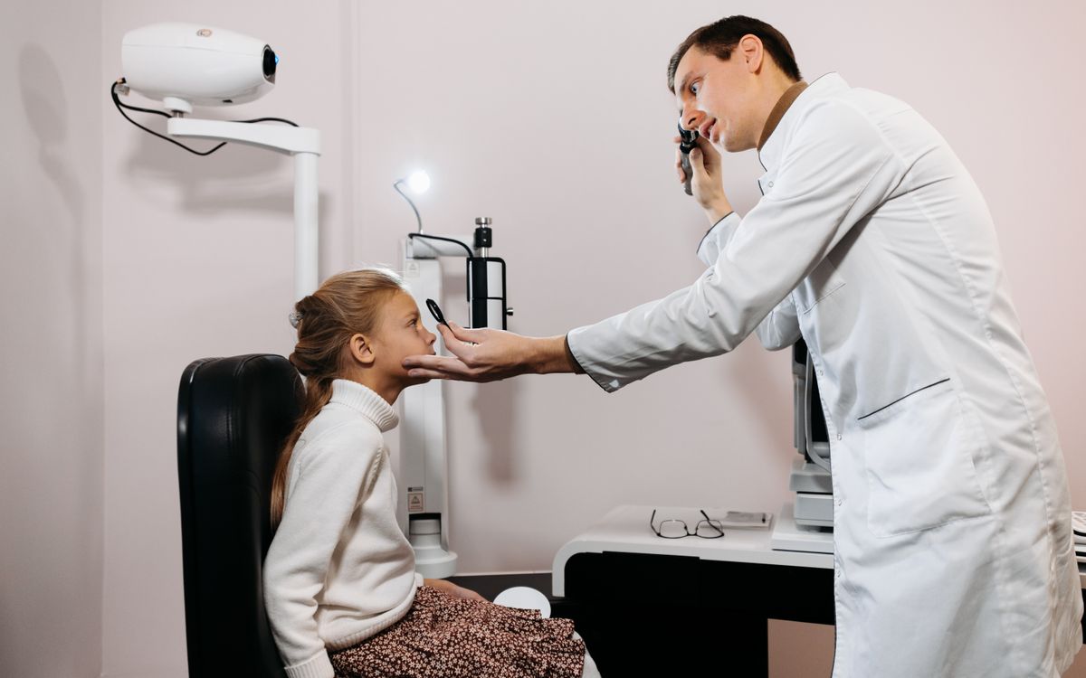 A medical professional performs an eye exam on a young girl in a clinic setting.