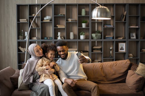 Free Delighted multiethnic family taking selfie sitting on couch Stock Photo