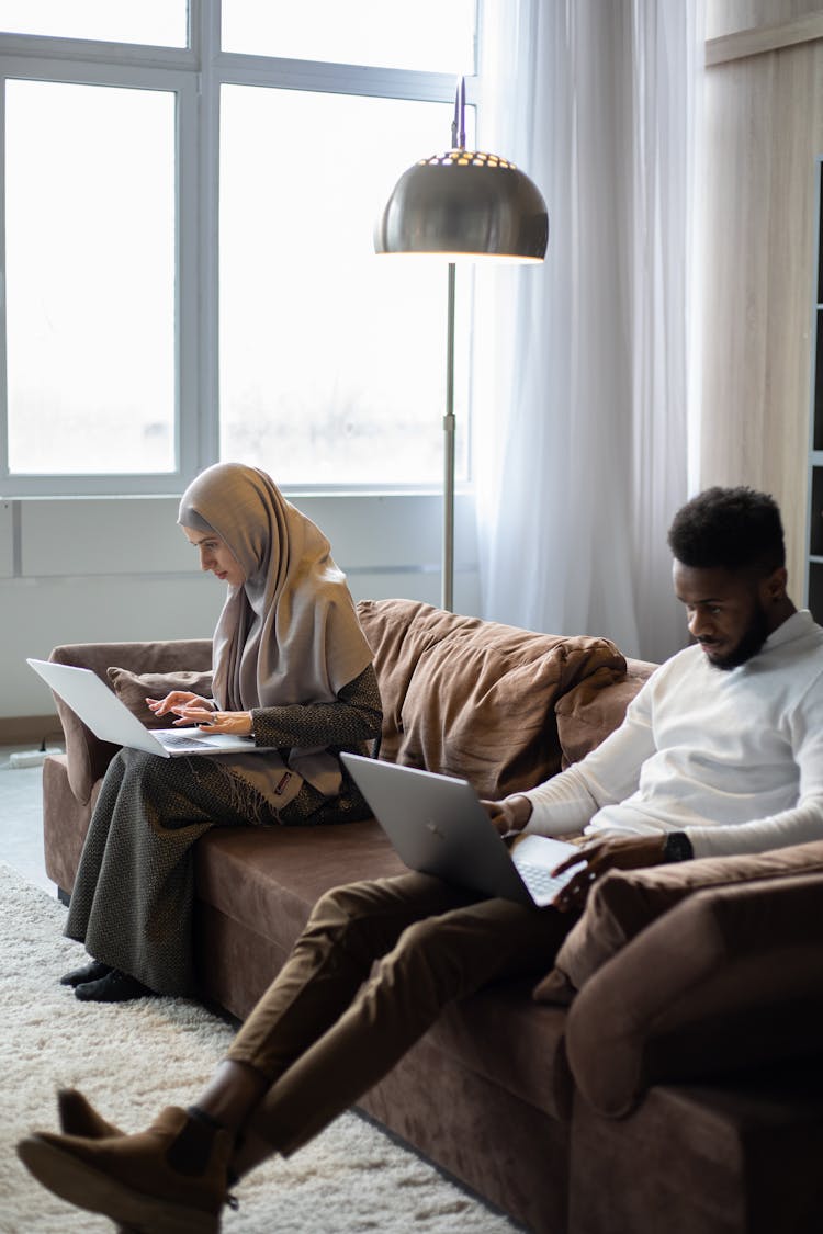 Multiethnic Couple Of Freelancers Working On Laptops On Sofa At Home