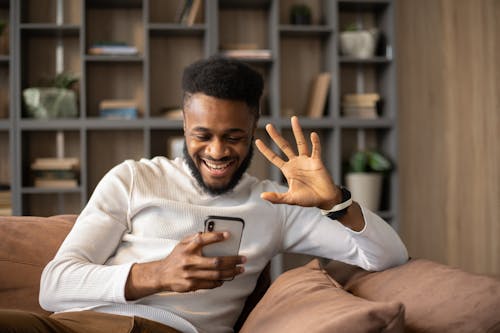 Cheerful black man having video call and waving hand