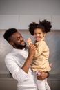 Delighted young African America father carrying adorable little daughter while having fun and looking at camera