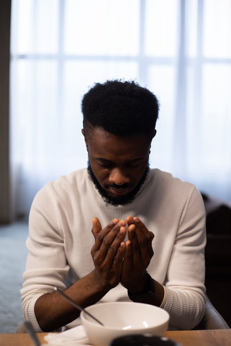 Thoughtful Black Man Praying At Table Before Eating