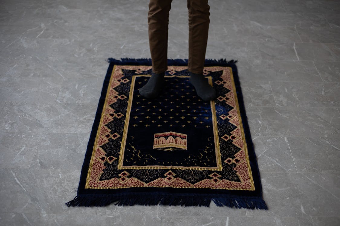 Free From above of crop anonymous male standing on prayer mat on floor at home before praying Stock Photo