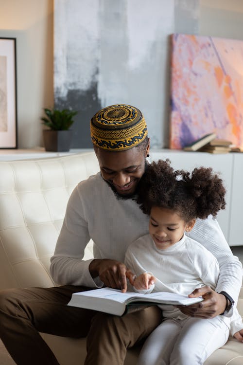 Free Delighted black father reading book to positive daughter Stock Photo