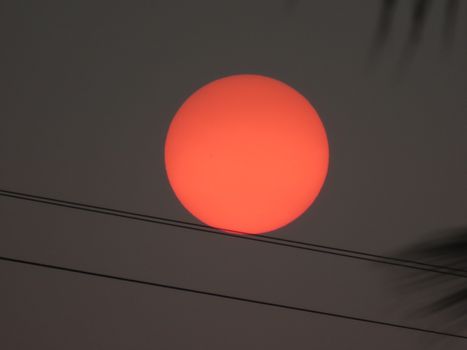 A striking red sun sets above electrical wires, captured in Mumbai, India.