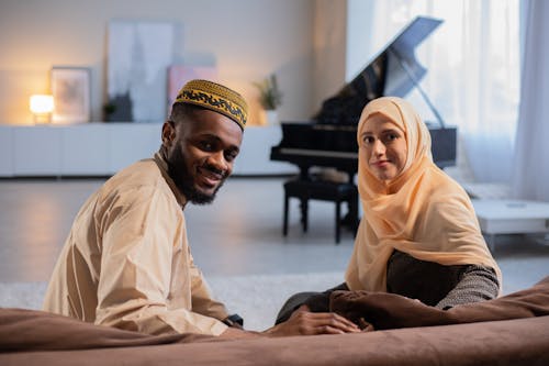 Satisfied black man and happy female in traditional muslim clothes looking at camera while having rest at home
