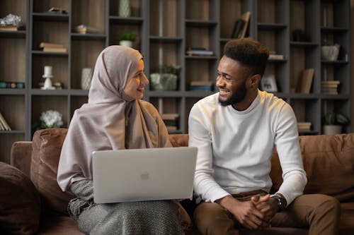 Positive female with laptop on lap and African American male looking at each other while spending time in living room