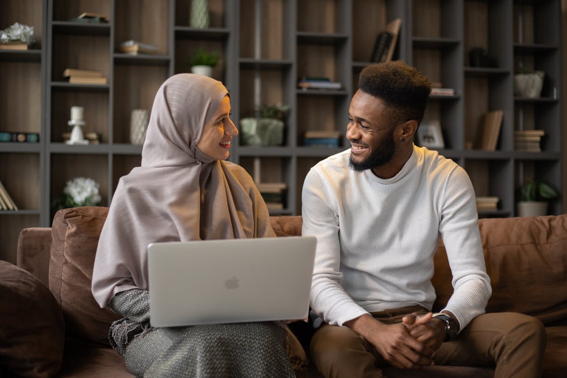 Positive female with laptop on lap and African American male looking at each other while spending time in living room