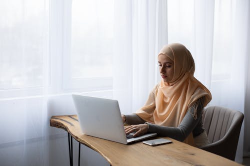 Macbook을 사용하여 테이블 옆에 앉아 갈색 Hijab 여자