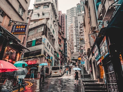 A bustling street in Hong Kong on a rainy day with people and umbrellas.