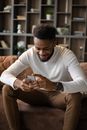 Positive black man using smartphone while sitting on sofa