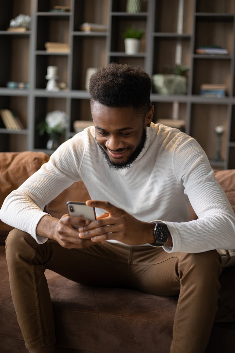 Positive Black Man Using Smartphone While Sitting On Sofa