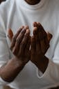 Selective focus of crop anonymous African American man wearing white turtleneck praying with open hands