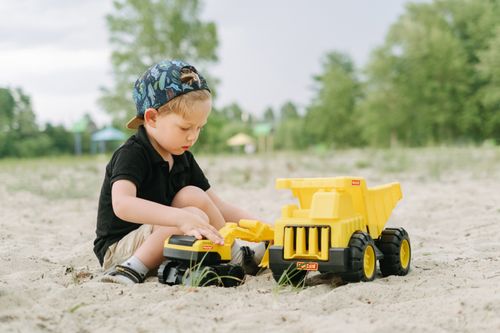 Free A young boy plays outdoors with a yellow toy truck in the sand, enjoying summertime fun. Stock Photo