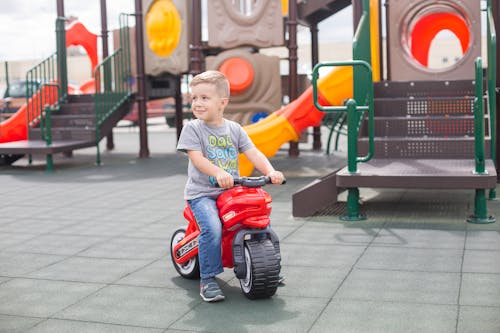 Free Boy Riding a Motorcycle Plastic Toy on Playground Stock Photo
