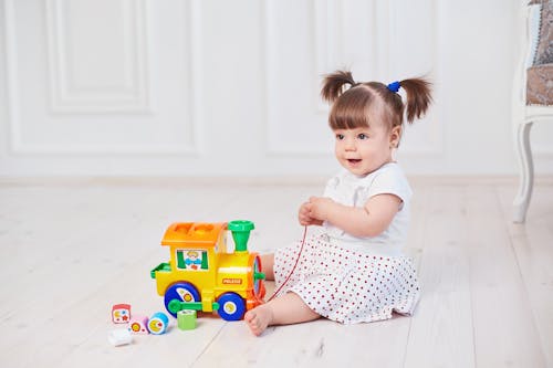 Free Baby Girl Sitting on the Floor Playing with the Toy Car Stock Photo