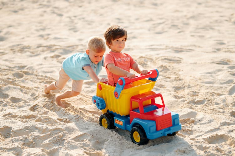 Two Boys Playing With A Toy Truck On Sand