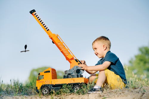 A Boy Sitting on Ground Playing Crane Truck Toy 