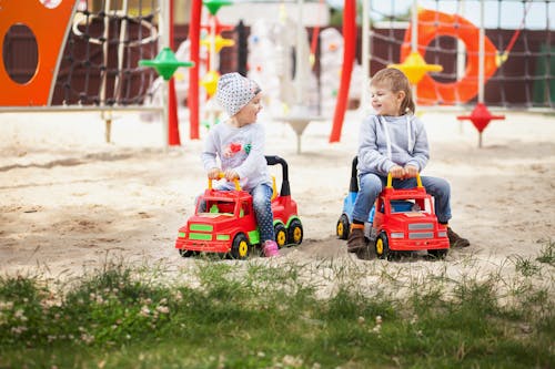 Children Riding Red Toy Cars on Playground